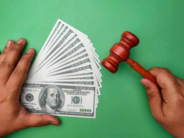 Gavel and hand holding banknotes on green background