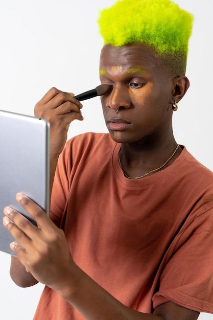 A gay black man putting on makeup LGTBI concept correcting blemishes with a mirror