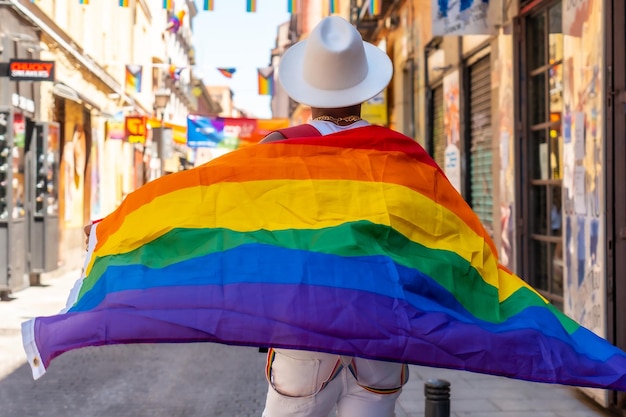 A gay black man walking in the pride party with an LGBT flag on his back