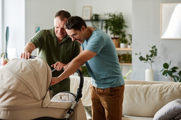 Gay couple standing with baby stroller in the room and caring about baby