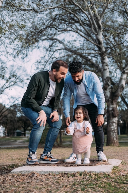 Gay couple with their young daughter enjoying a day in a park dancing happily