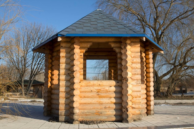 Gazebo made of wooden logs against the sky and trees