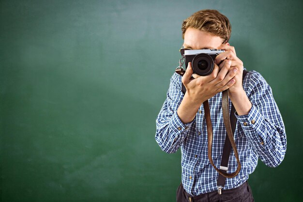 Photo geeky hipster holding a retro camera against green chalkboard