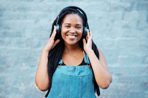 Gen z black woman music headphones and portrait on wall background in Nigeria city listening to radio audio and sound Happy young african girl student freedom and streaming urban outdoor podcast