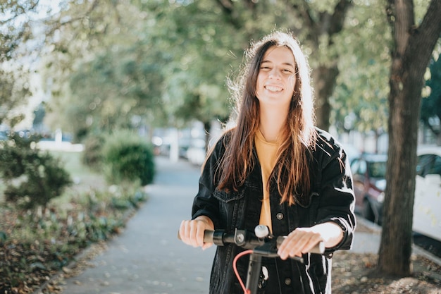 Gen z young people using electric scooter in city park with copy space during a sunset