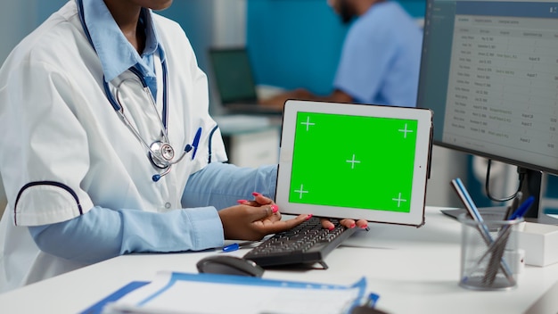 General practitioner showing horizontal greenscreen on tablet, meeting with patient wheelchair user. Using isolated chroma key template with blank mockup display and copyspace. Close up.