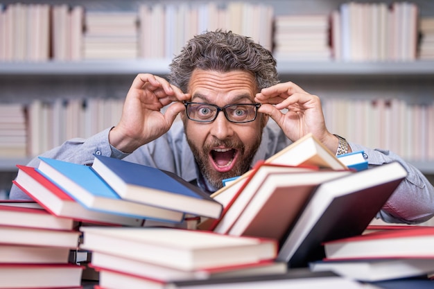 Photo genius studying homework literature near pile of books man teacher read book school education in college knowledge day overwork of bookworm teacher genius in school library research education