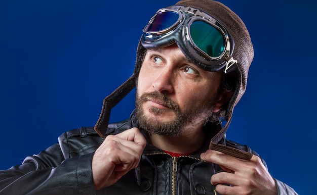 Photo gentleman pilot of the 20s with sunglasses and vintage aviator helmet. wears leather jacket, beard and expressive faces