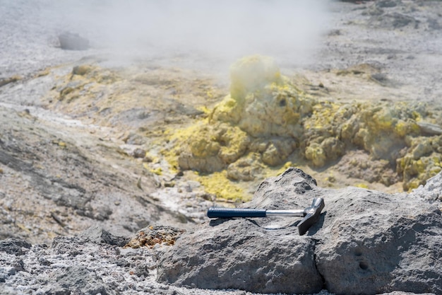 Geological hammer on the rock against the backdrop of an steaming fumarole on the slope of a volcano