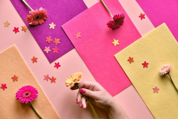 Geometric two tone flat lay on paper and felt geometric layered background. Gerbera flower in hand and floral confetti.