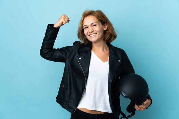 Georgian girl holding a motorcycle helmet isolated on blue background doing strong gesture