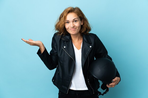 Georgian girl holding a motorcycle helmet isolated on blue background having doubts while raising hands