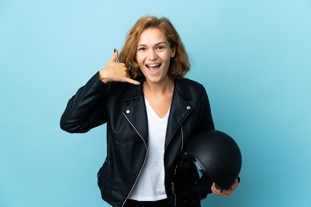 Georgian girl holding a motorcycle helmet isolated on blue background making phone gesture. Call me back sign