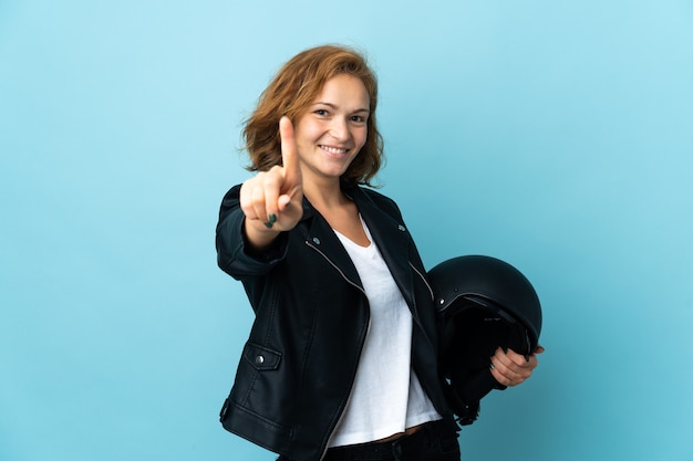 Georgian girl holding a motorcycle helmet isolated on blue background showing and lifting a finger