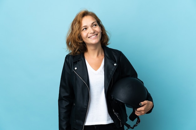 Georgian girl holding a motorcycle helmet isolated on blue background thinking an idea while looking up