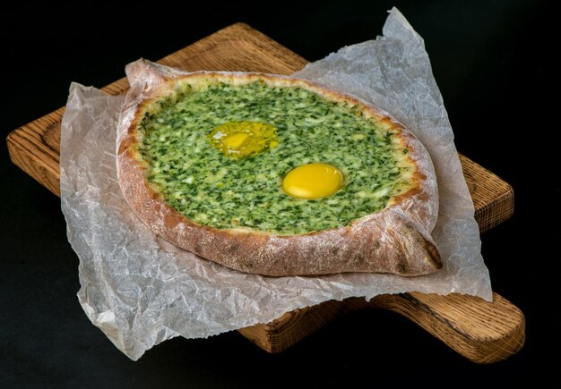 Georgian khachapuri with egg and cheese national traditional cuisine on a black plate on wooden background.