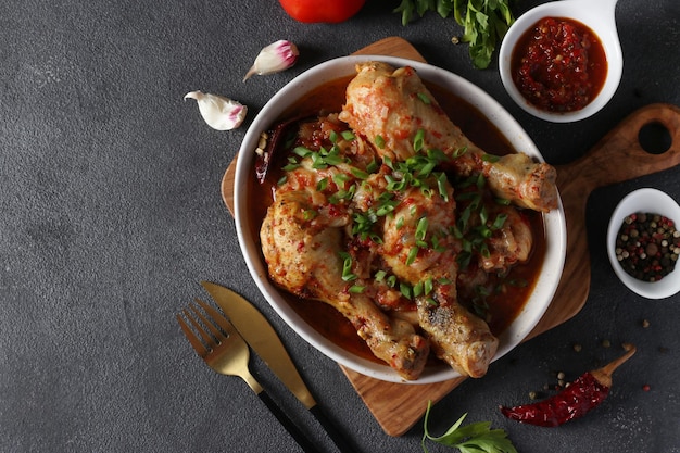 Georgian meat dish chashushuli with chicken and tomato on wooden board on dark gray table