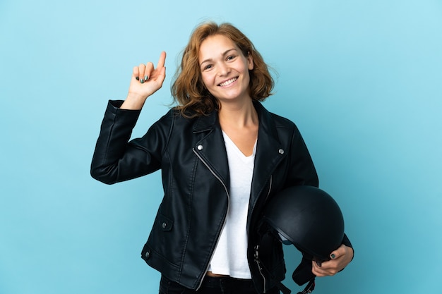 Georgian woman holding a motorcycle helmet isolated on blue wall pointing up a great idea