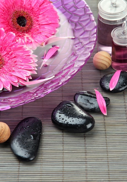 Gerbera flowers on water and spa stones on bamboo mat