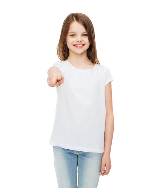 gestures and happy people concept - happy little girl in blank white t-shirt pointing at you