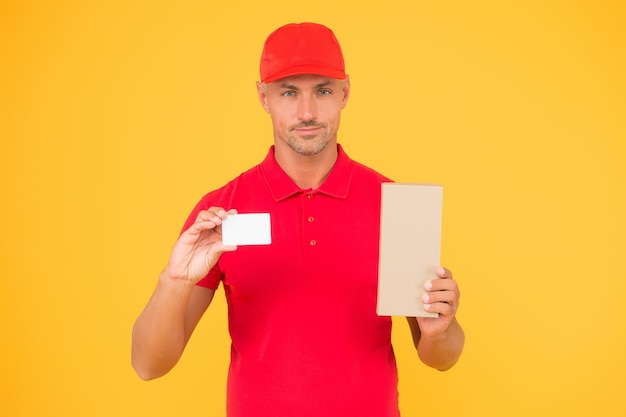 Get free discount card. Delivered to your destination. Service delivery. Courier and delivery. Postman delivery worker. Handsome man red cap yellow background. Delivering purchase. Business contact.