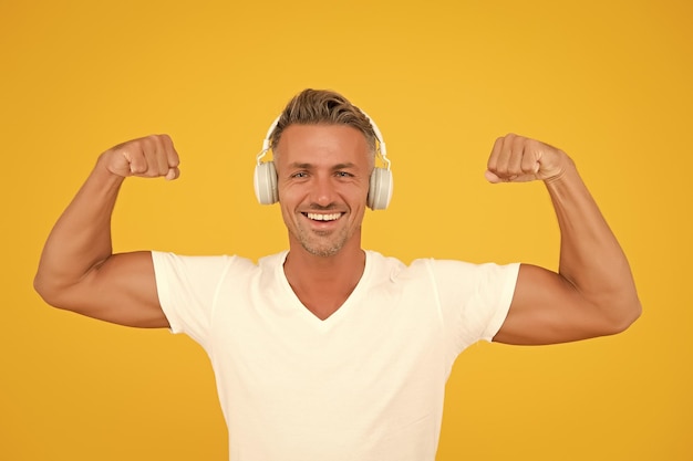 Get powerful sounds Strong man flex arms yellow background Headphones technology Modern workout and training Force and strength Strong music experience