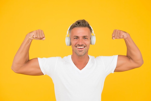 Get powerful sounds. Strong man flex arms yellow background. Headphones technology. Modern workout and training. Force and strength. Strong music experience.