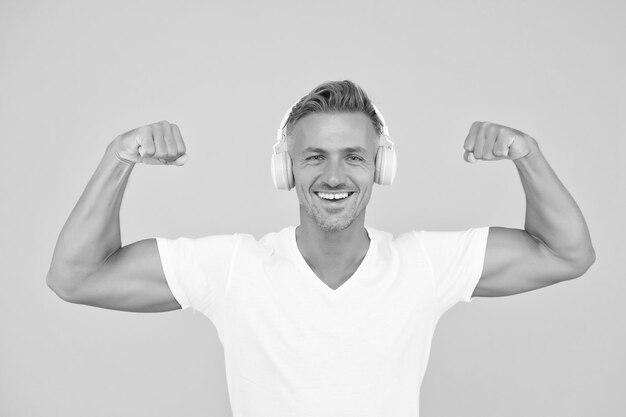 Get powerful sounds Strong man flex arms yellow background Headphones technology Modern workout and training Force and strength Strong music experience