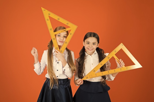 Getting back to the square roots Little girls ready for geometry lesson Small girls are back to school School children with measuring instruments Cute schoolgirls holding triangles for lesson