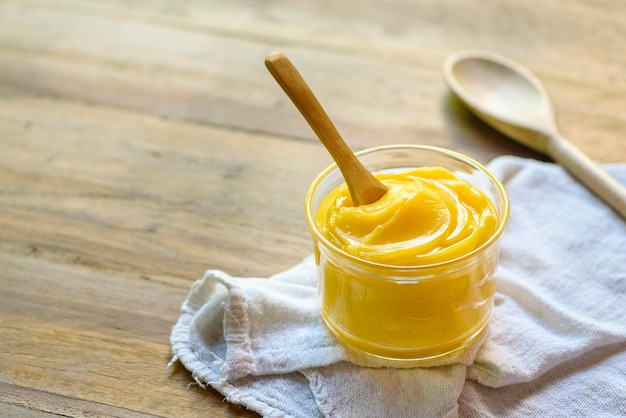 Ghee butter in glass jar with wooden spoon on wooden table with blurred background