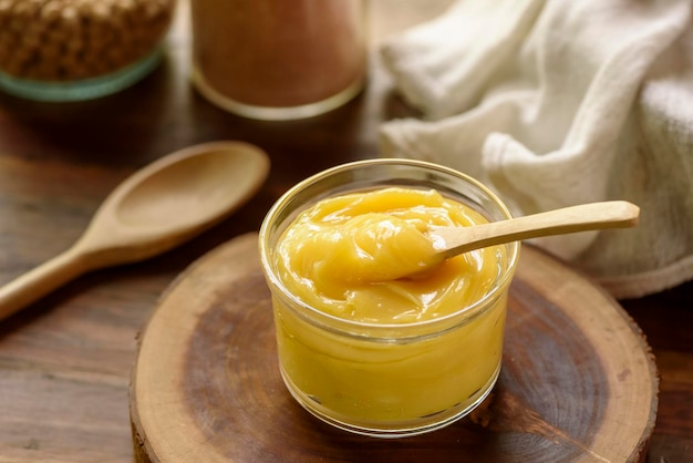 Ghee butter in glass jar with wooden spoon on wooden table with blurred background