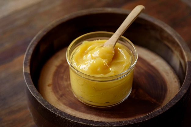 Ghee butter in glass jar with wooden spoon on wooden table with blurred background