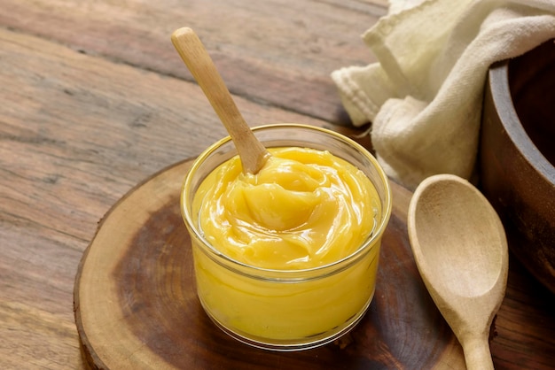 Ghee butter in glass jar with wooden spoon on wooden table with blurred background