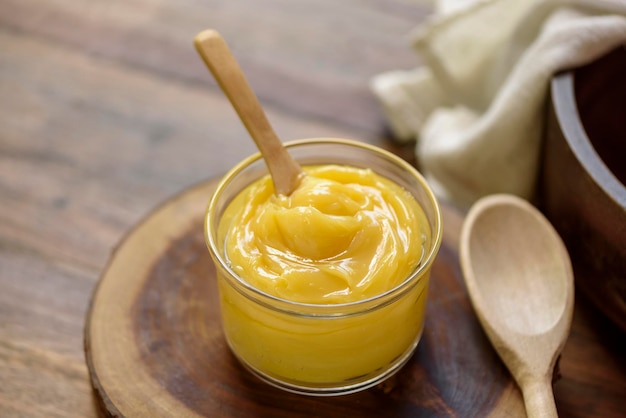 Ghee butter in glass jar with wooden spoon on wooden table with blurred background