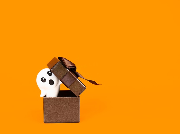 a ghost peeks out of a gift box on an orange background