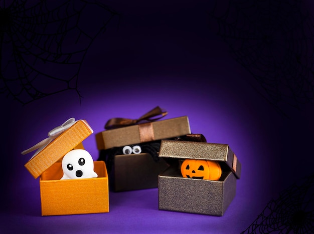 ghost, spider and pumpkin peeking out of boxes on dark purple background