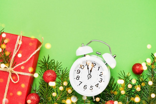 Gift box alarm clock and christmas decoration on green background copy space