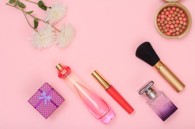 Gift box, bottles with perfume, brush, lipstick and powder on a pink background. Women cosmetics and accessories. Top view.