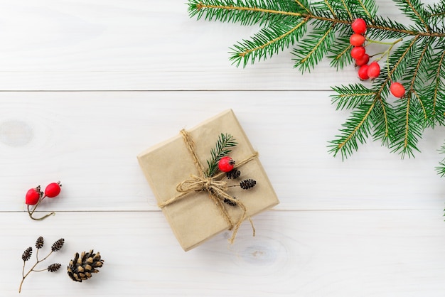 Gift in a box for Christmas and New Year with a fir branch and cones on a wooden table.