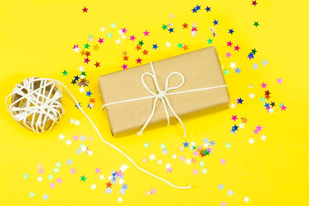 gift box and colorful stars confetti on yellow background christmas holiday concept