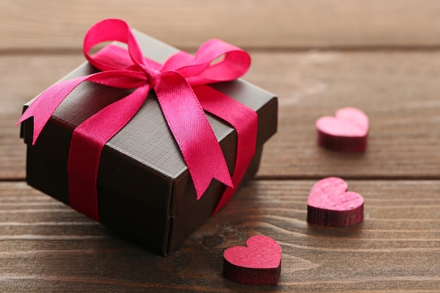 Gift box and decorative hearts on wooden background