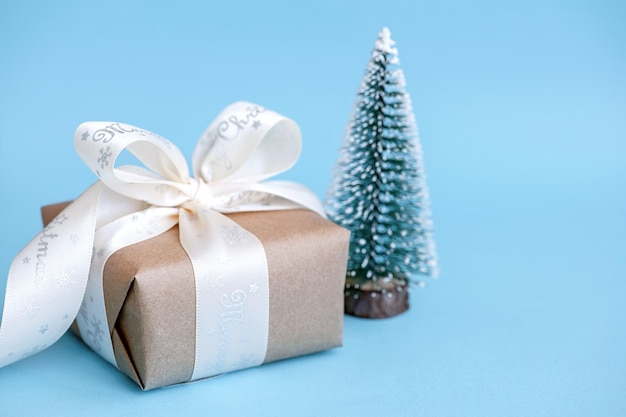 Gift box and miniature Christmas tree on a blue background. Festive composition