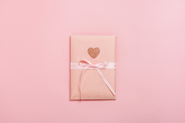 Gift box package with heart on pastel pink background.