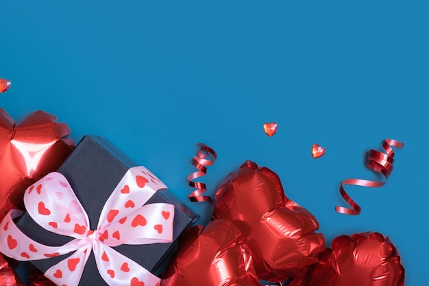 Gift box and red heart shape baloons on blue background Valentines Day greeting card Copy space