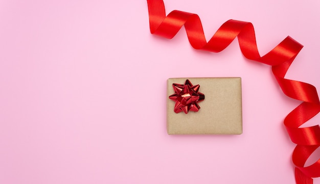 Gift box and red satin ribbon on the side on a pink background