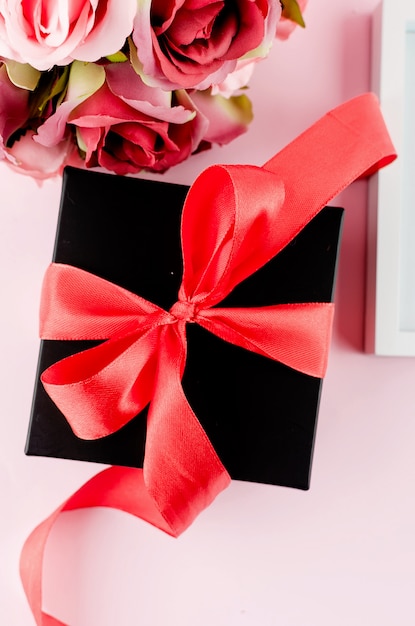 Gift box, roses and empty frame on a pink background