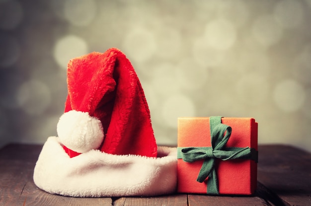 Gift box and santa claus hat on wooden table with bokeh on background