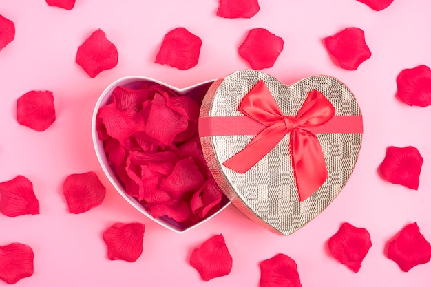 Photo gift box in the shape of a heart with rose petals inside on a pink background happy valentine's day concept