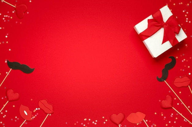 Gift box and soft hearts lips and paper moustache over red background. Template of Valentine's day