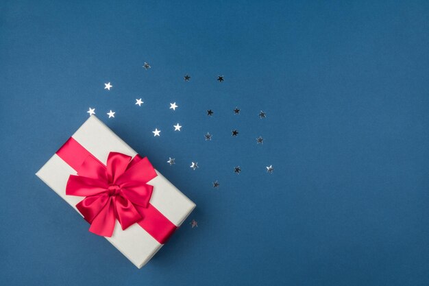 Gift box with big red bow on blue background with silver sequins